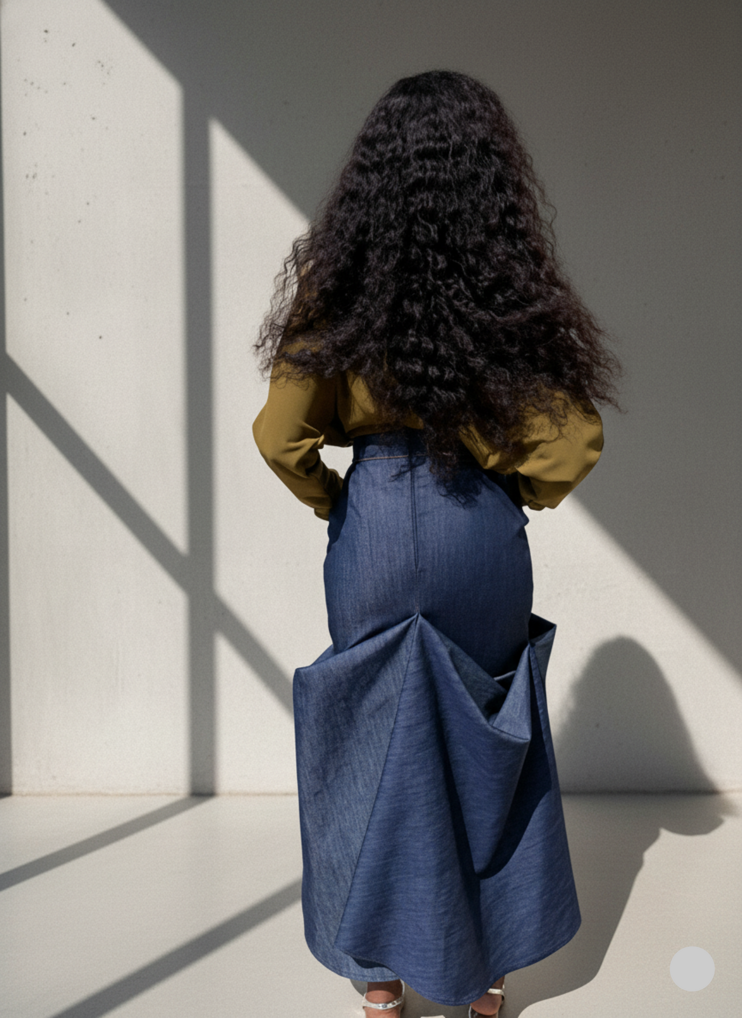 Person wearing a long denim skirt with a plain background