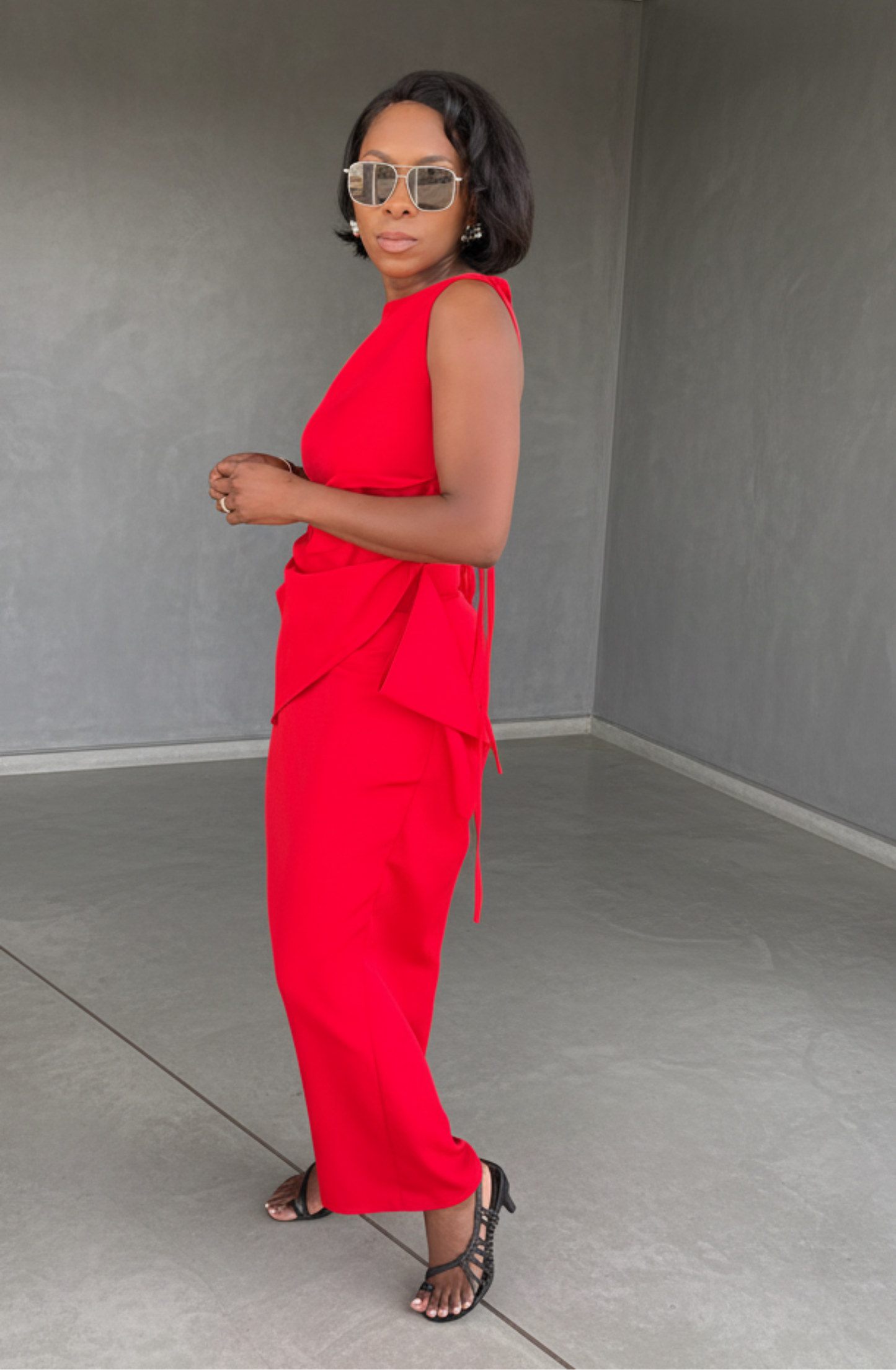 Woman in a red outfit standing in an empty room with gray walls and floor.
