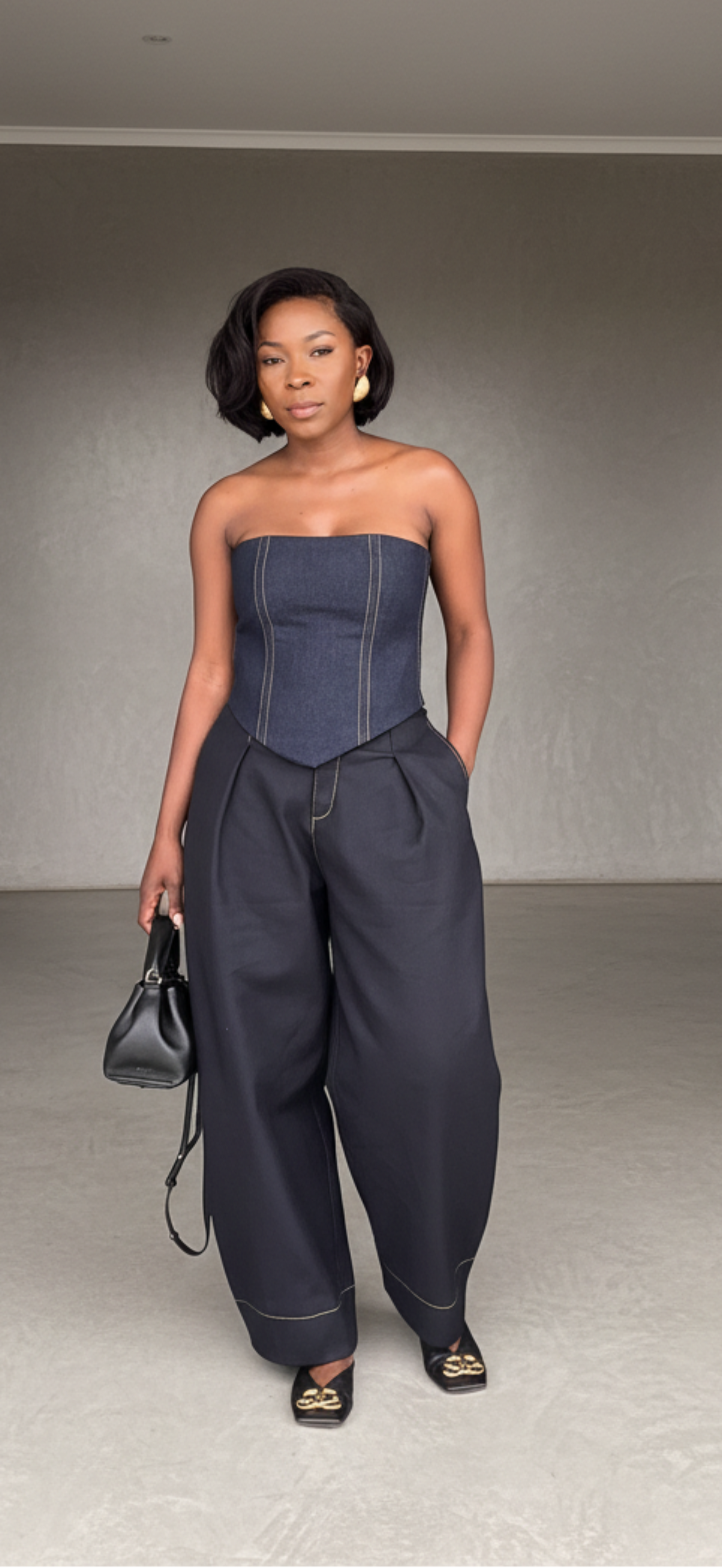 Woman in a strapless top and high-waisted pants standing in a minimalistic room.