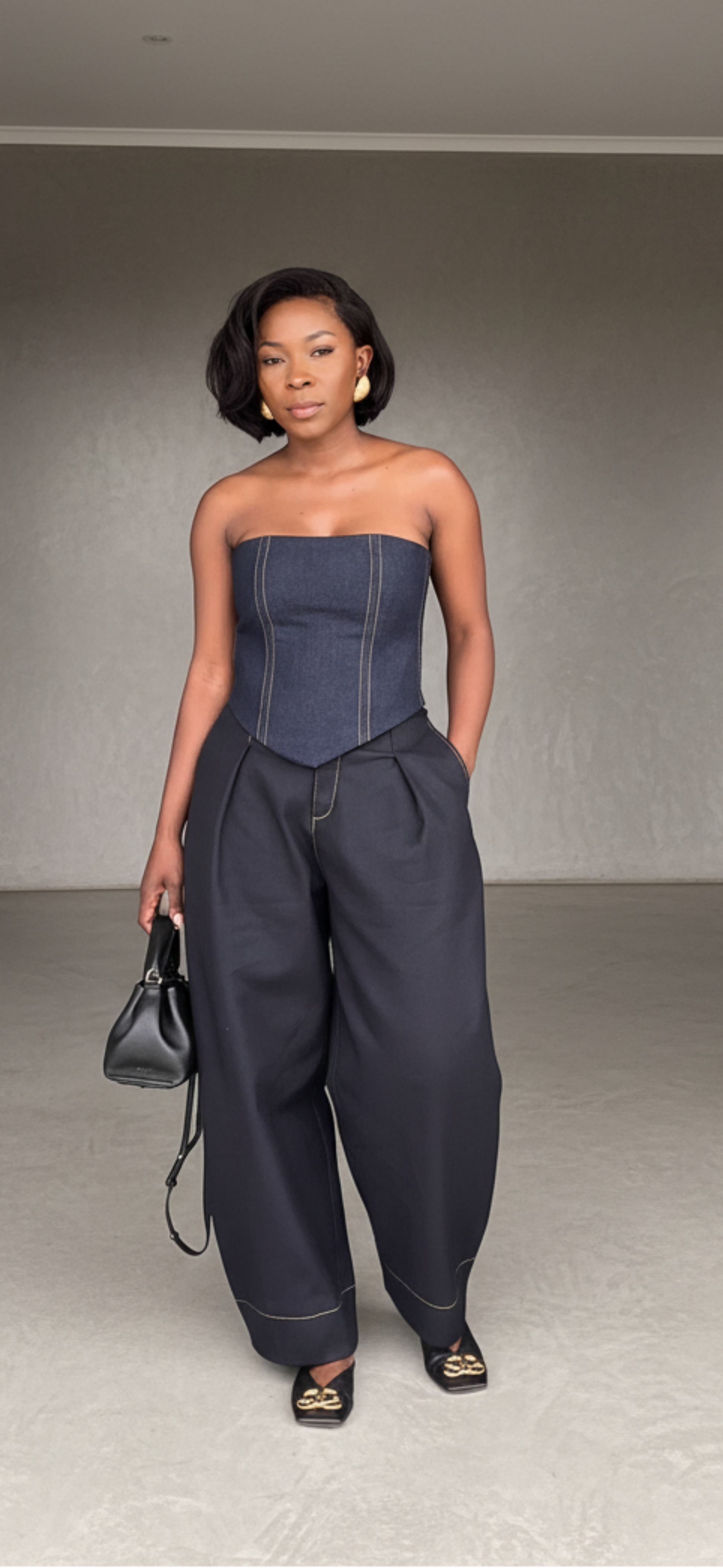 Woman in a strapless top and high-waisted pants standing in a minimalistic room.