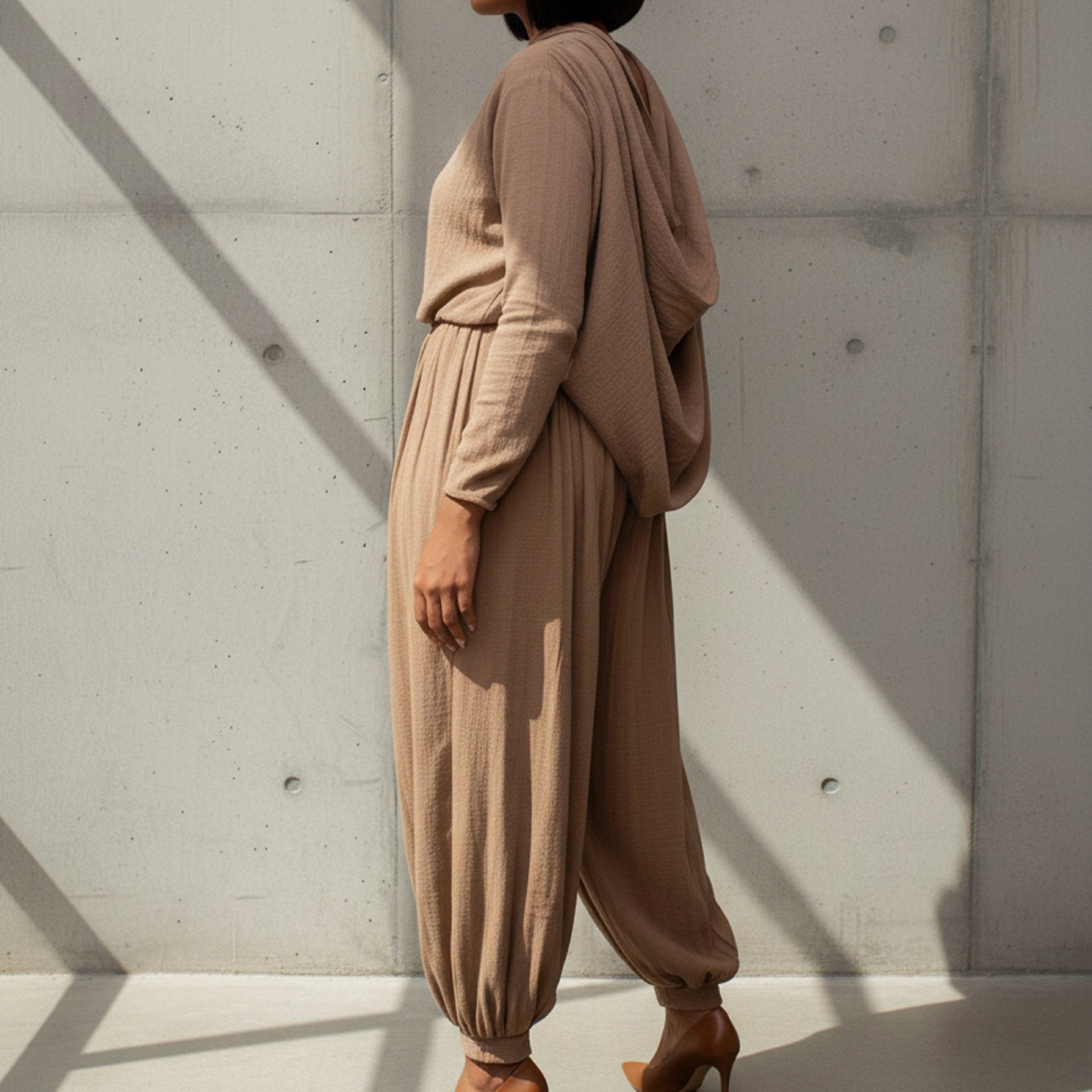 Person wearing a beige outfit standing against a light gray wall.