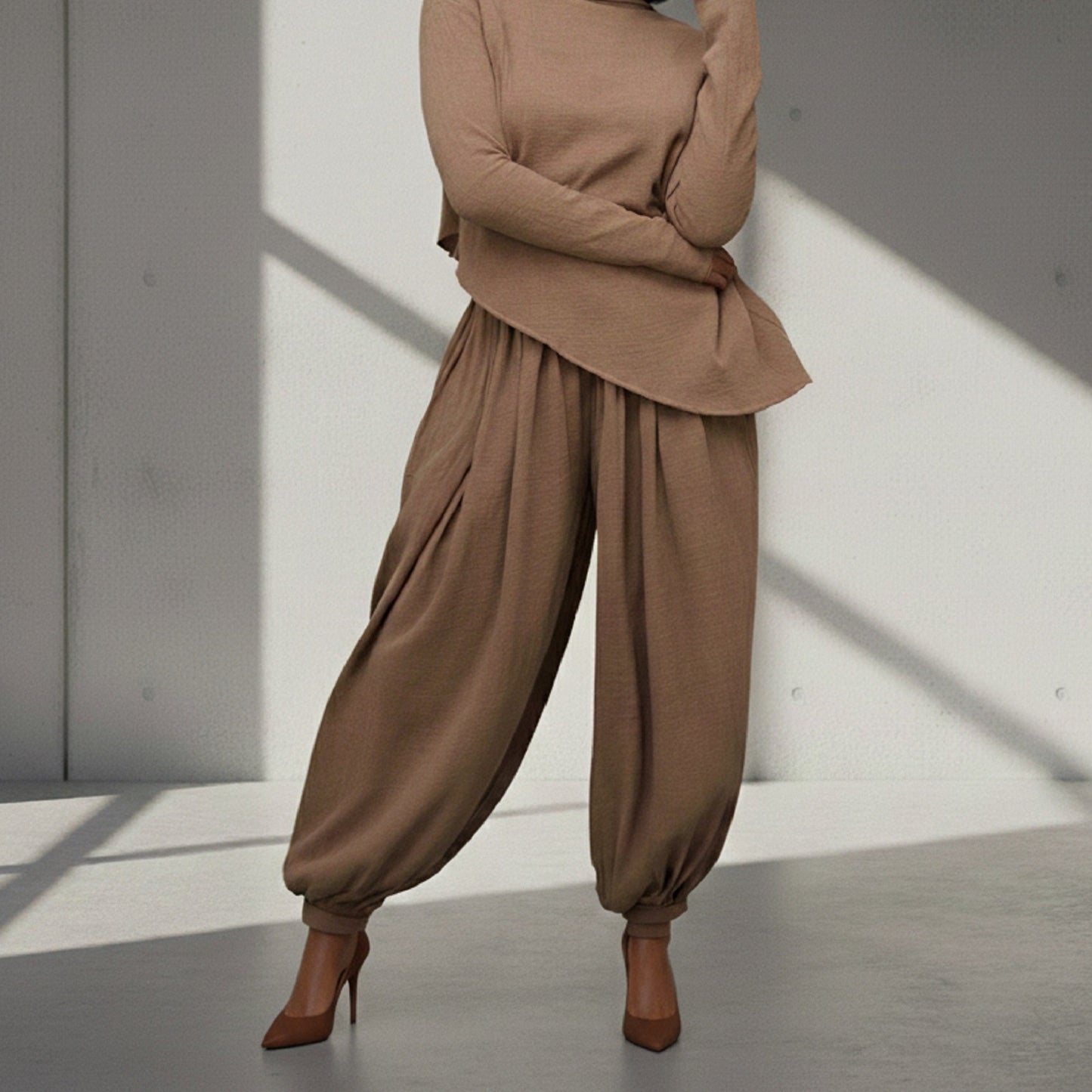 Person wearing a brown outfit with wide-leg pants and high heels in a minimalistic setting