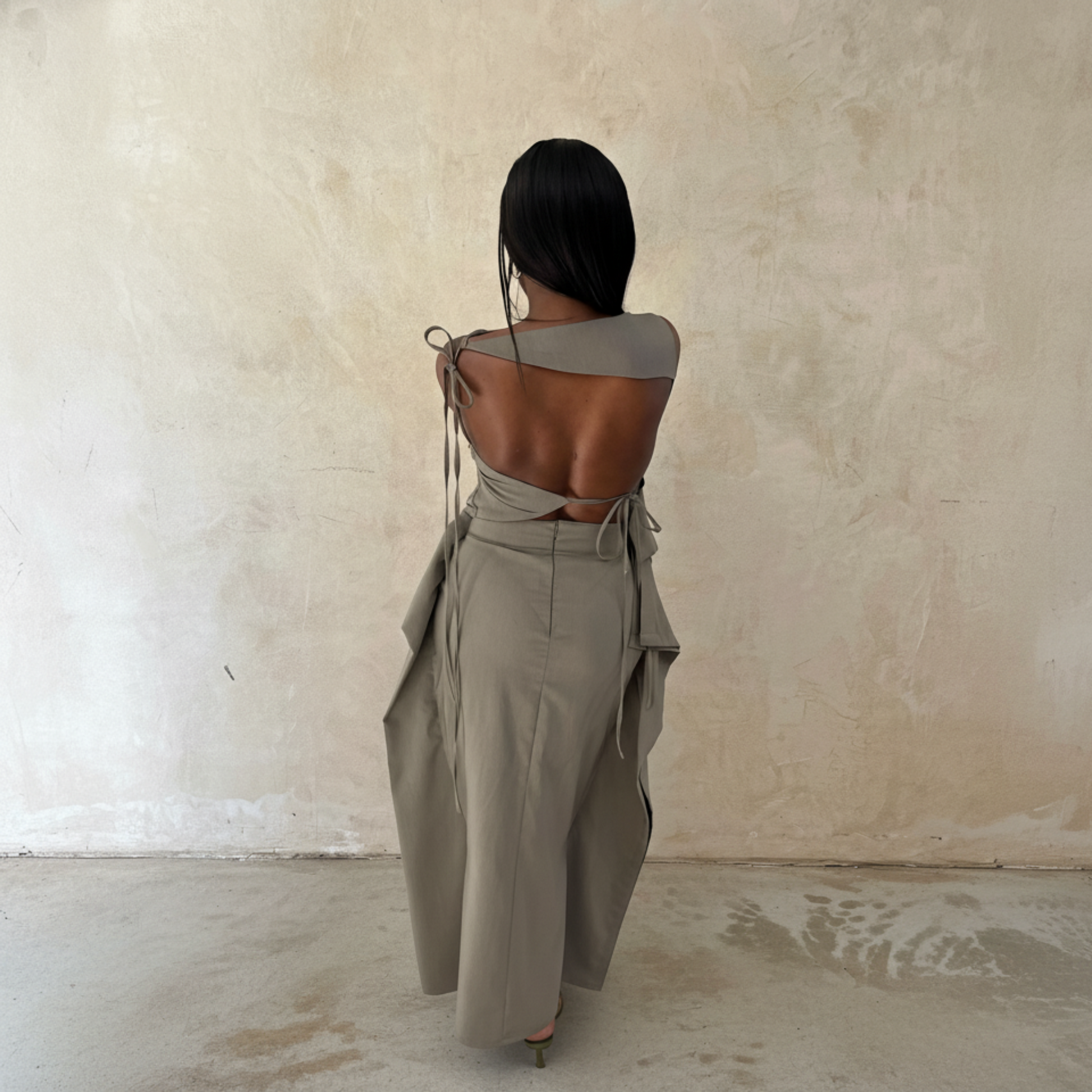 Person wearing a stylish outfit with a unique back design against a plain wall.