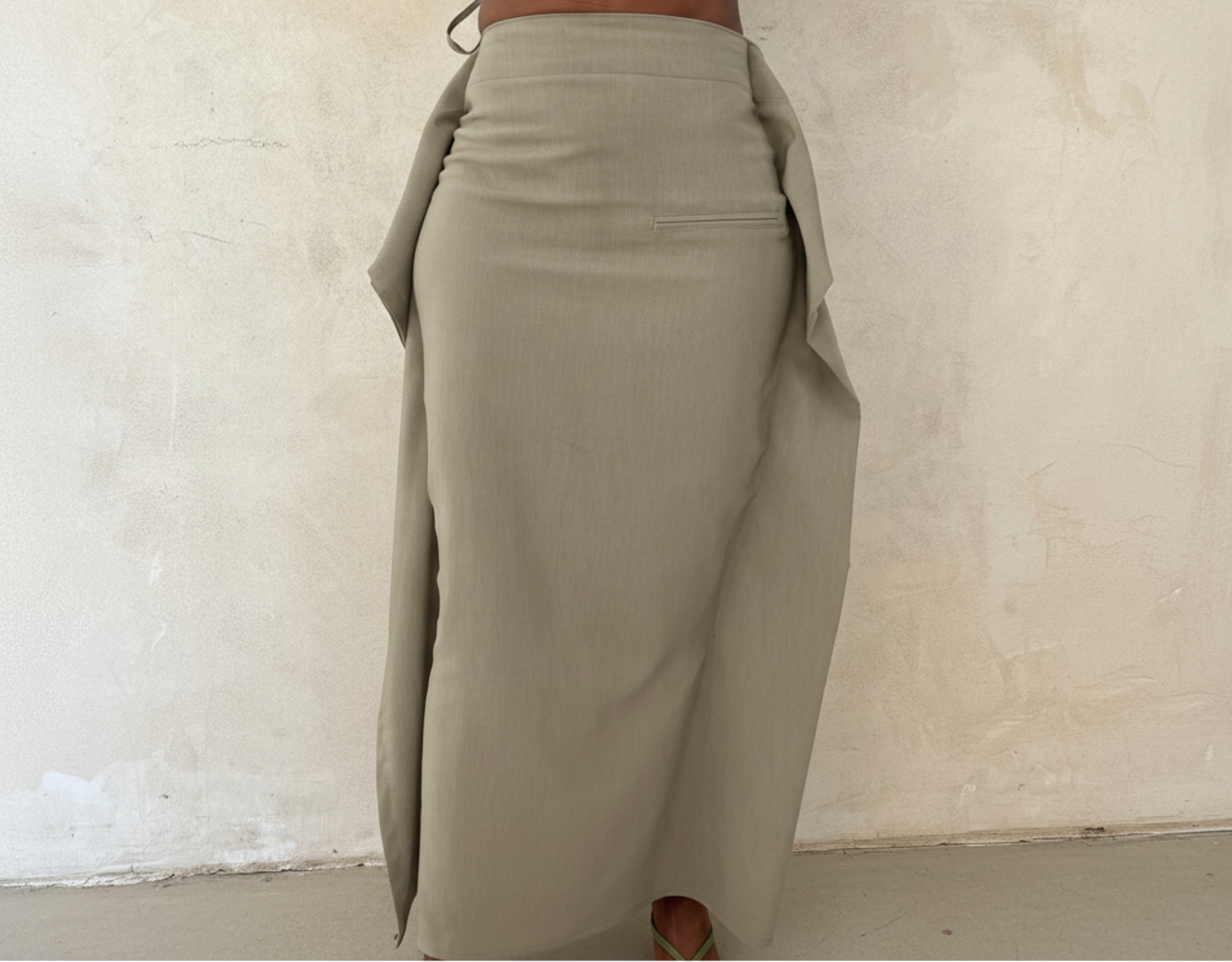 Person wearing a light green outfit with wide-leg pants against a textured white wall.